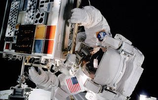 An astronaut mounts a previous version of the MISSE hardware to the International Space Station during a spacewalk.